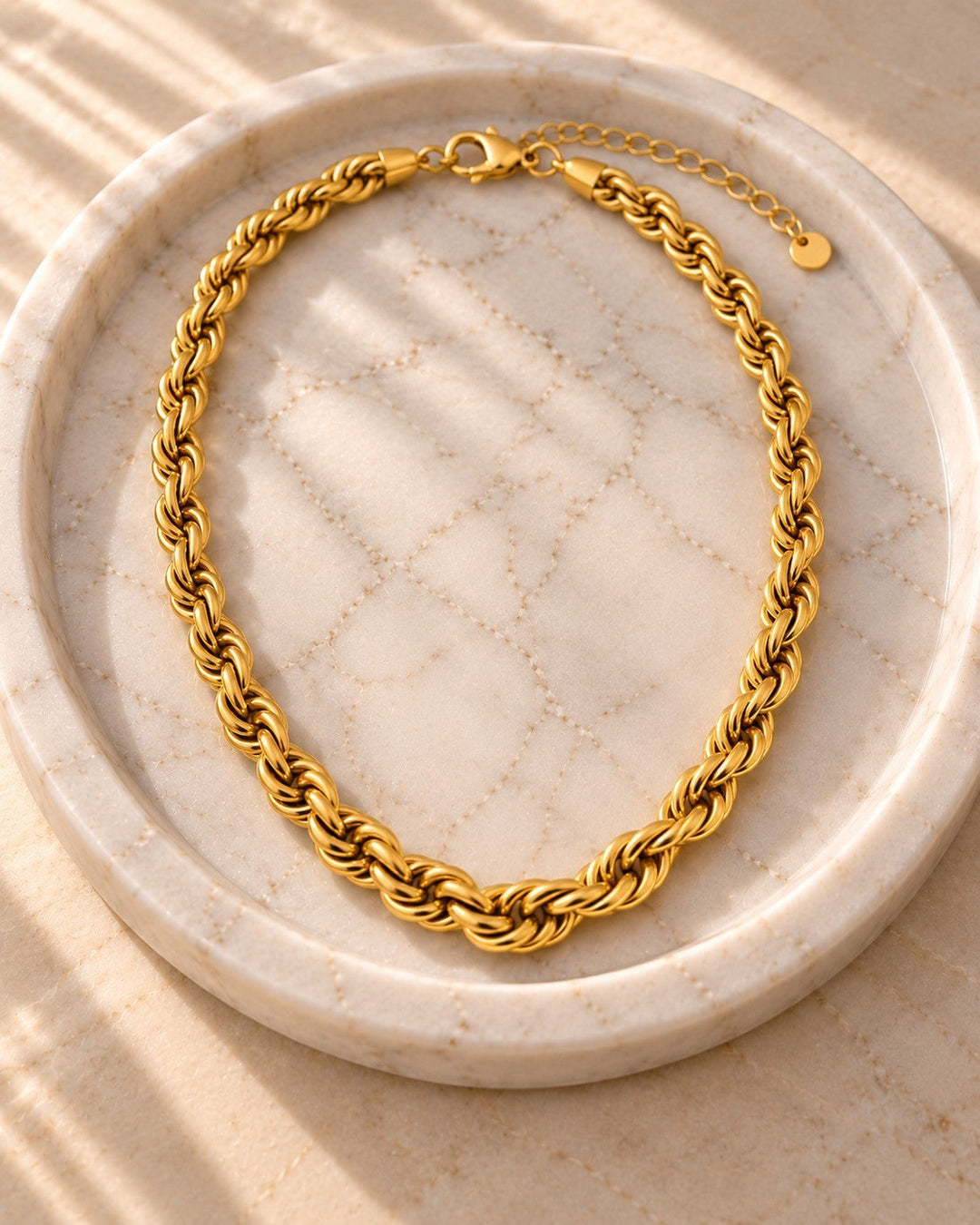 Elli Jewellery gold plated chunky rope chain necklace resting on a textured marble tray in warm sunlight.