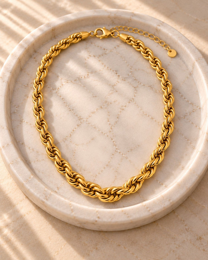 Elli Jewellery gold plated chunky rope chain necklace resting on a textured marble tray in warm sunlight.