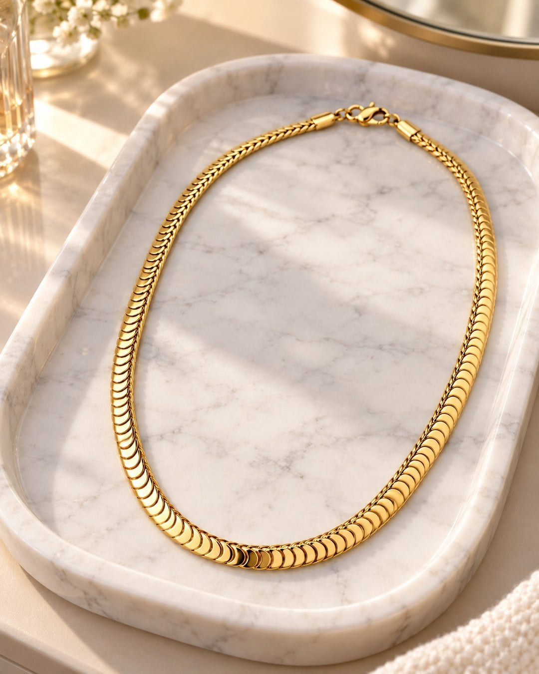 Elli Jewellery gold plated chunky snake chain necklace resting on a white marble tray in soft sunlight.