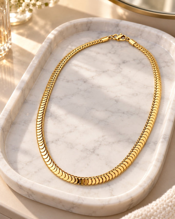 Elli Jewellery gold plated chunky snake chain necklace resting on a white marble tray in soft sunlight.
