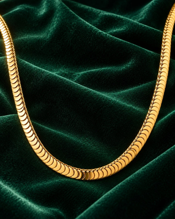 Elli Jewellery gold plated chunky snake chain necklace resting on a luxurious dark green velvet background.