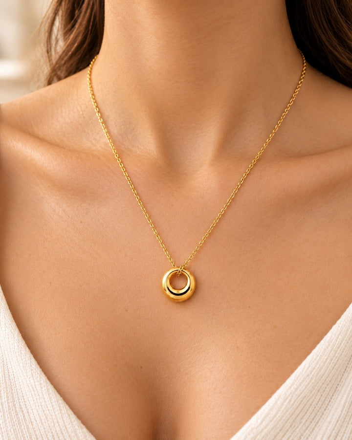 Elli Jewellery gold plated waterproof circle pendant necklace worn on a model with a white top