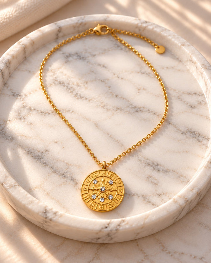 Elli Jewellery gold plated compass coin pendant necklace with crystal accents on a marble tray