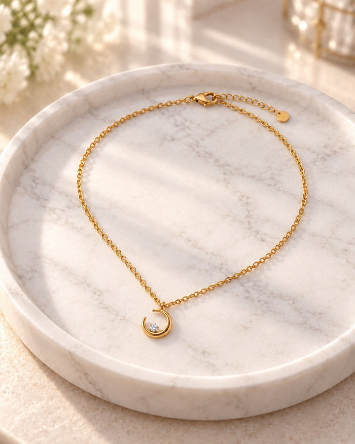 Elli Jewellery gold plated waterproof crescent moon pendant necklace with a delicate chain on a marble tray