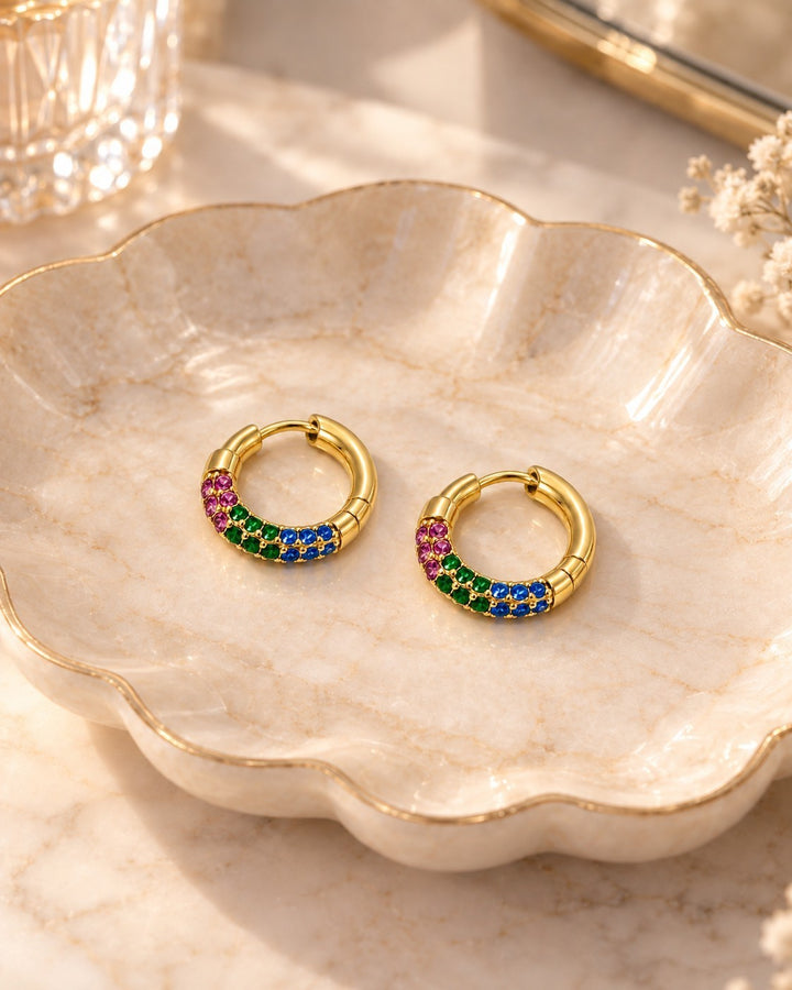 Elli Jewellery gold plated hoop earrings featuring vibrant multicoloured crystal stones on a decorative ceramic dish.