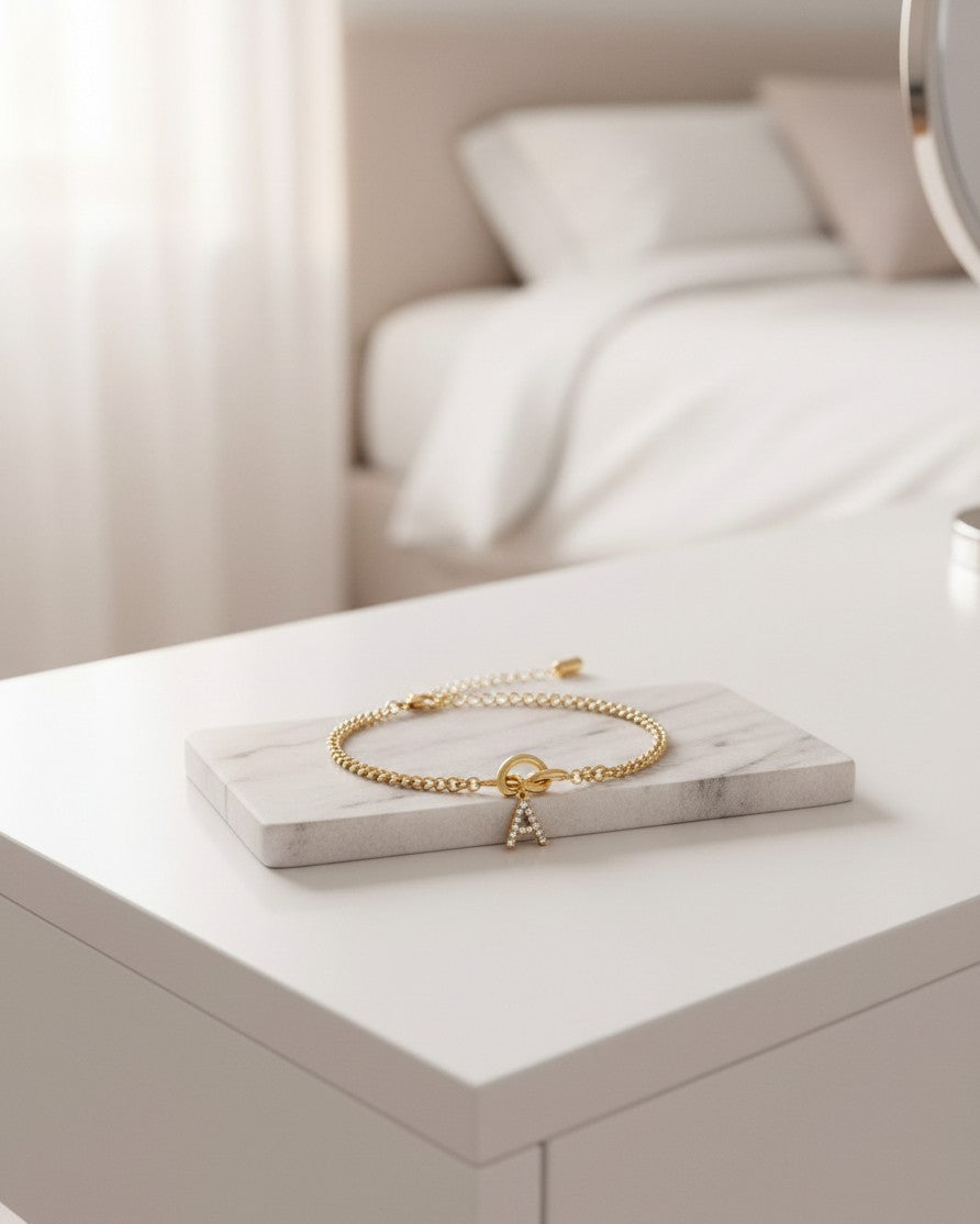 Elli Jewellery gold-plated initial bracelet with a crystal-encrusted letter A charm on a marble display stand.