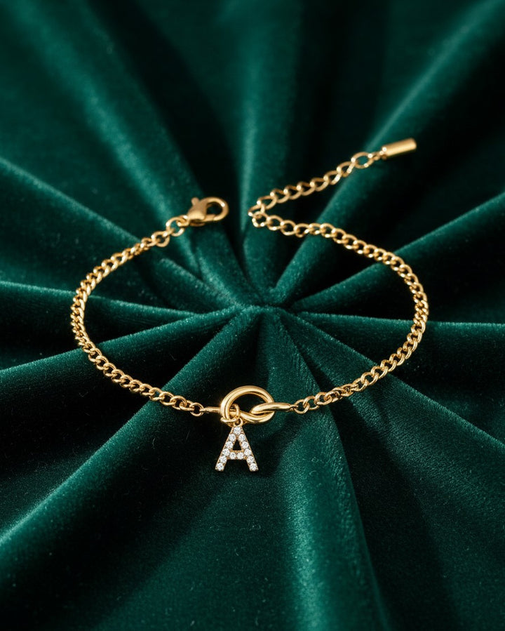 Elli Jewellery gold plated chain bracelet featuring a crystal embellished letter A charm on green velvet background