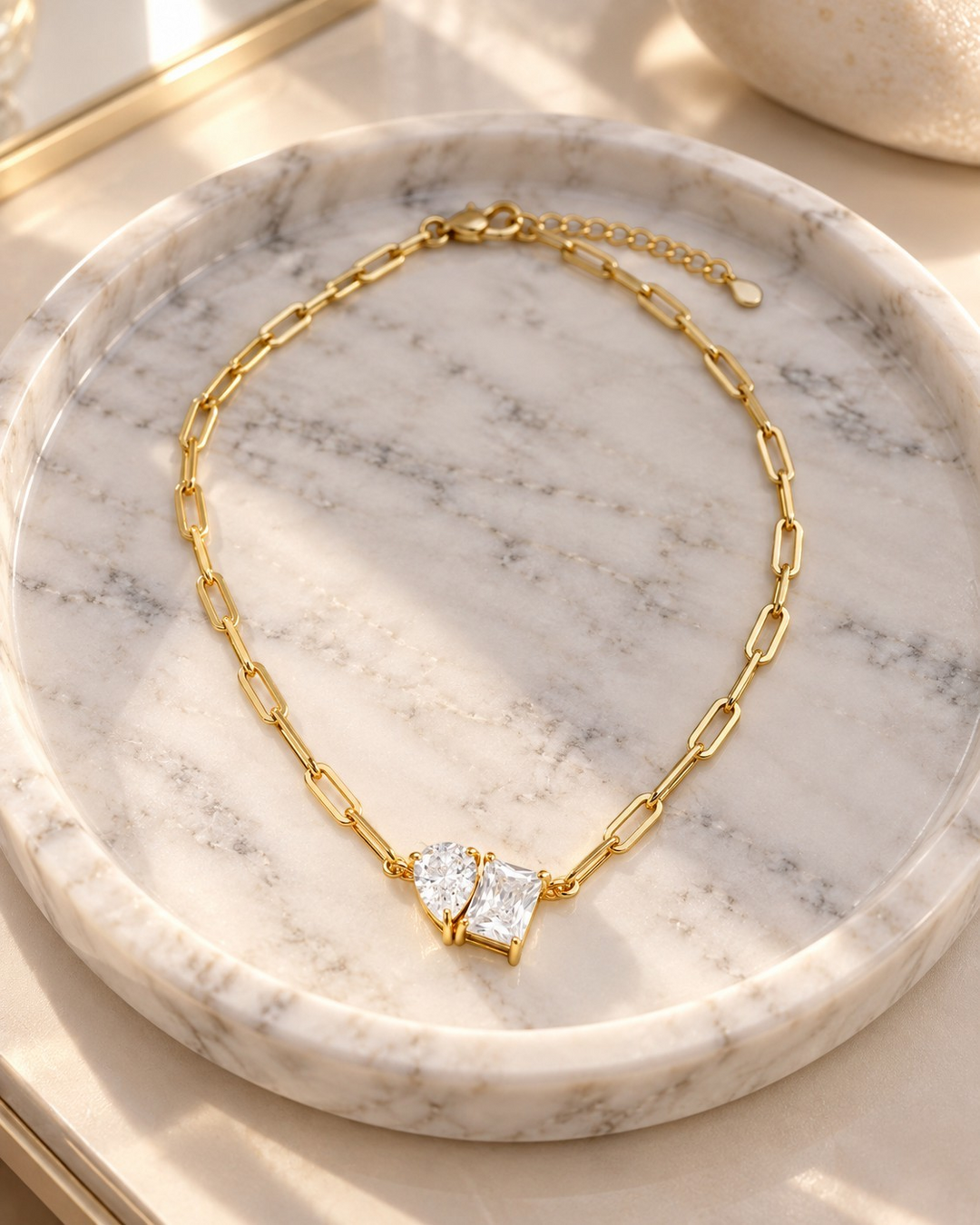 Elli Jewellery gold-plated paper clip chain necklace with a rectangle and pear-shaped crystal pendant on marble tray.