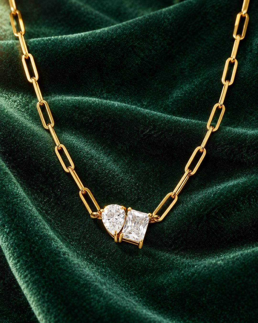 Elli Jewellery gold-plated paper clip chain necklace featuring a pear and rectangle crystal pendant on green velvet.