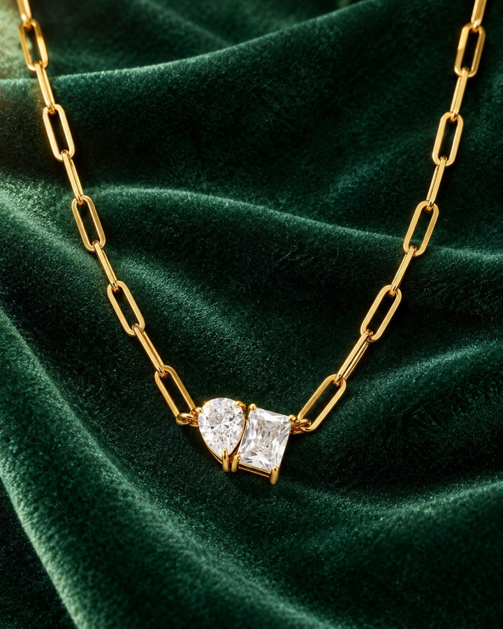Elli Jewellery gold-plated paper clip chain necklace featuring a pear and rectangle crystal pendant on green velvet.