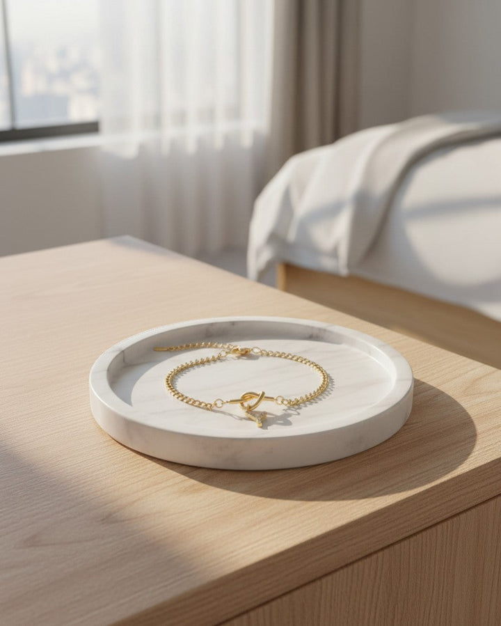 Elli Jewellery gold plated crystal Y initial charm bracelet on a white marble tray in a sunlit bedroom.