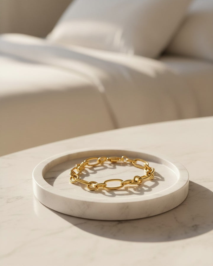 Elli Jewellery gold plated waterproof Cuban link chain bracelet resting on a white marble tray in a bright bedroom.