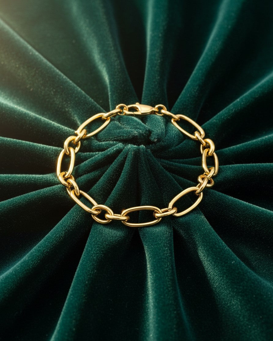 Elli Jewellery gold plated waterproof Cuban link chain bracelet resting on a dark green velvet fabric background.