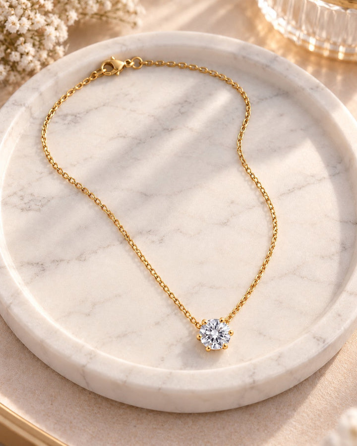 Elli Jewellery gold plated solitaire necklace with a sparkling cubic zirconia pendant on a marble tray.