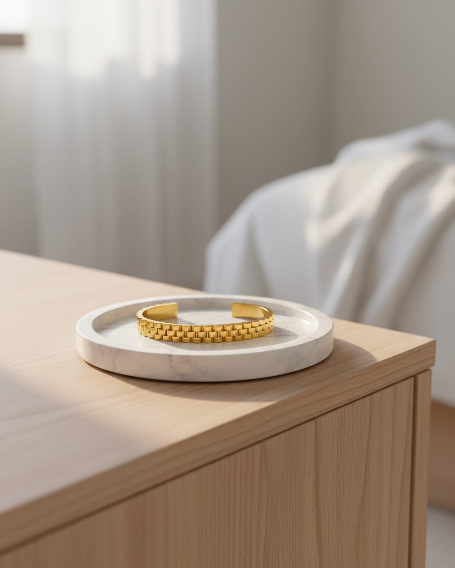 Elli Jewellery gold plated waterproof wide cuff bangle with a textured link design resting on a marble tray.