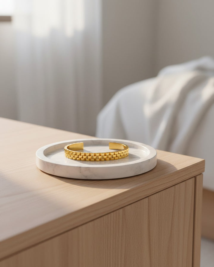 Elli Jewellery gold plated waterproof wide cuff bangle with a textured link design resting on a marble tray.