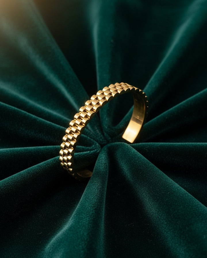 Elli Jewellery gold plated waterproof wide cuff bangle with a textured link design resting on dark green velvet.