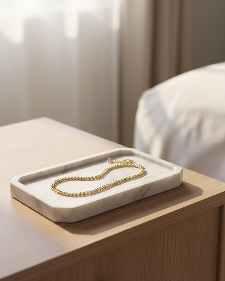 Elli Jewellery gold plated waterproof curb chain bracelet resting on a white marble tray on a wooden bedside table.