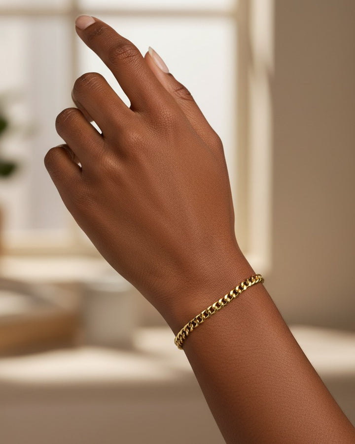 Elli Jewellery gold plated waterproof curb chain bracelet worn on a woman's wrist in a bright, minimalist setting.
