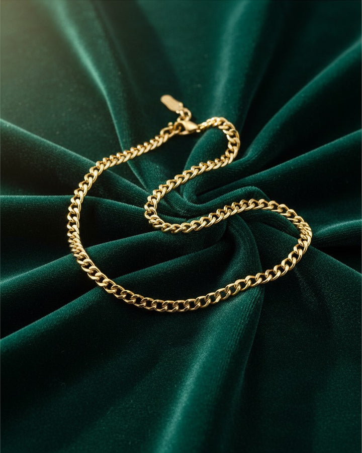 Elli Jewellery gold plated waterproof curb chain bracelet resting on a luxurious dark green velvet background.
