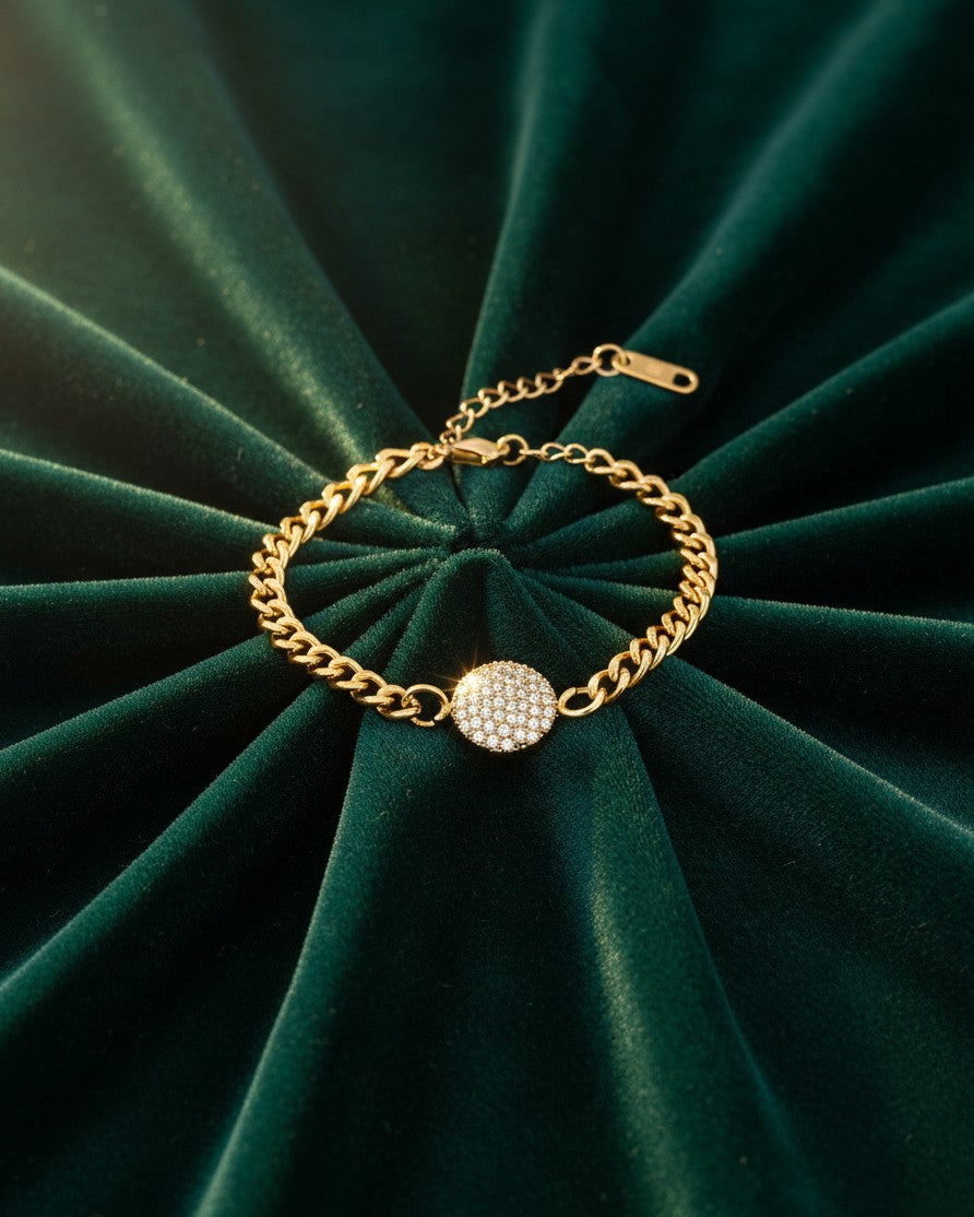 Elli Jewellery gold plated curb chain bracelet featuring a round diamanté pendant on a dark green velvet background.