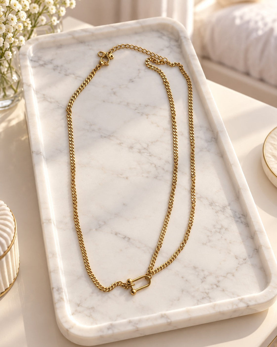 Elli Jewellery gold plated waterproof half layered curb chain necklace with a unique shackle clasp on a marble tray.