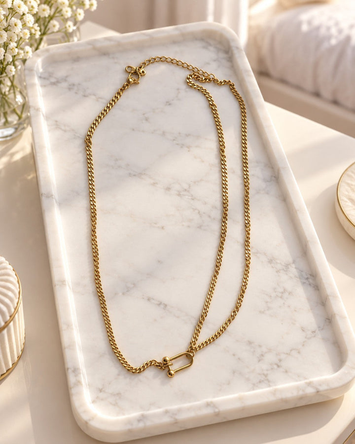 Elli Jewellery gold plated waterproof half layered curb chain necklace with a unique shackle clasp on a marble tray.