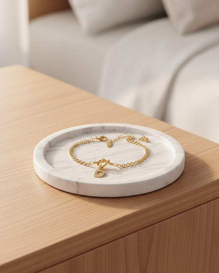 Elli Jewellery gold plated waterproof bracelet with a crystal diamante D initial charm on a marble tray.