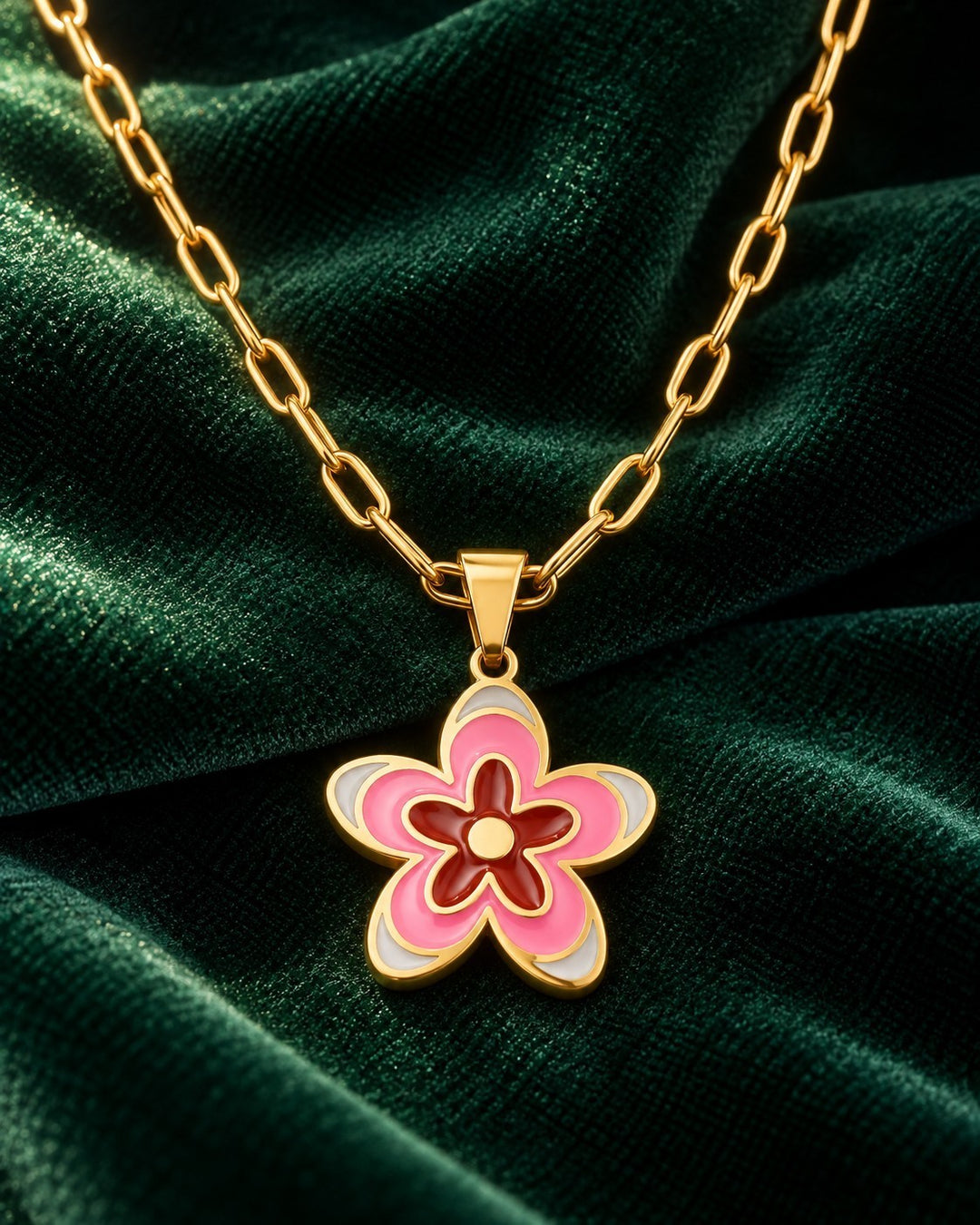 Elli Jewellery gold plated daisy flower pendant necklace with pink and red enamel on a gold chain against green velvet