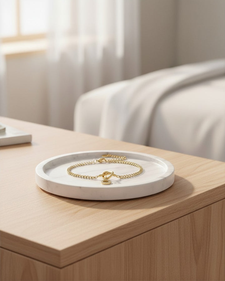 Elli Jewellery gold plated chain bracelet with a diamanté O-ring charm resting on a white marble tray.