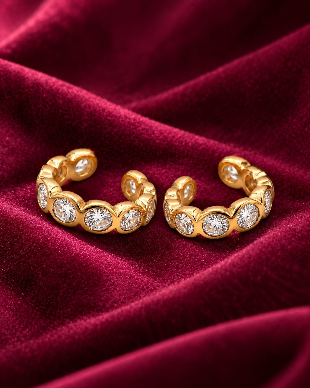 Elli Jewellery gold plated cuff earrings featuring sparkling diamanté crystals on a rich red velvet background.