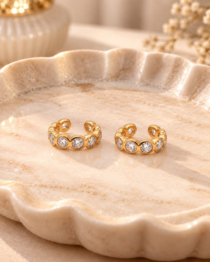 Elli Jewellery gold plated cuff earrings featuring sparkling diamanté crystals on a polished marble tray