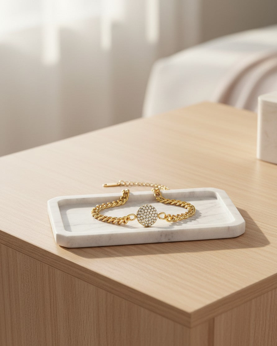 Elli Jewellery gold plated curb chain bracelet with a round diamanté pendant resting on a white marble tray.