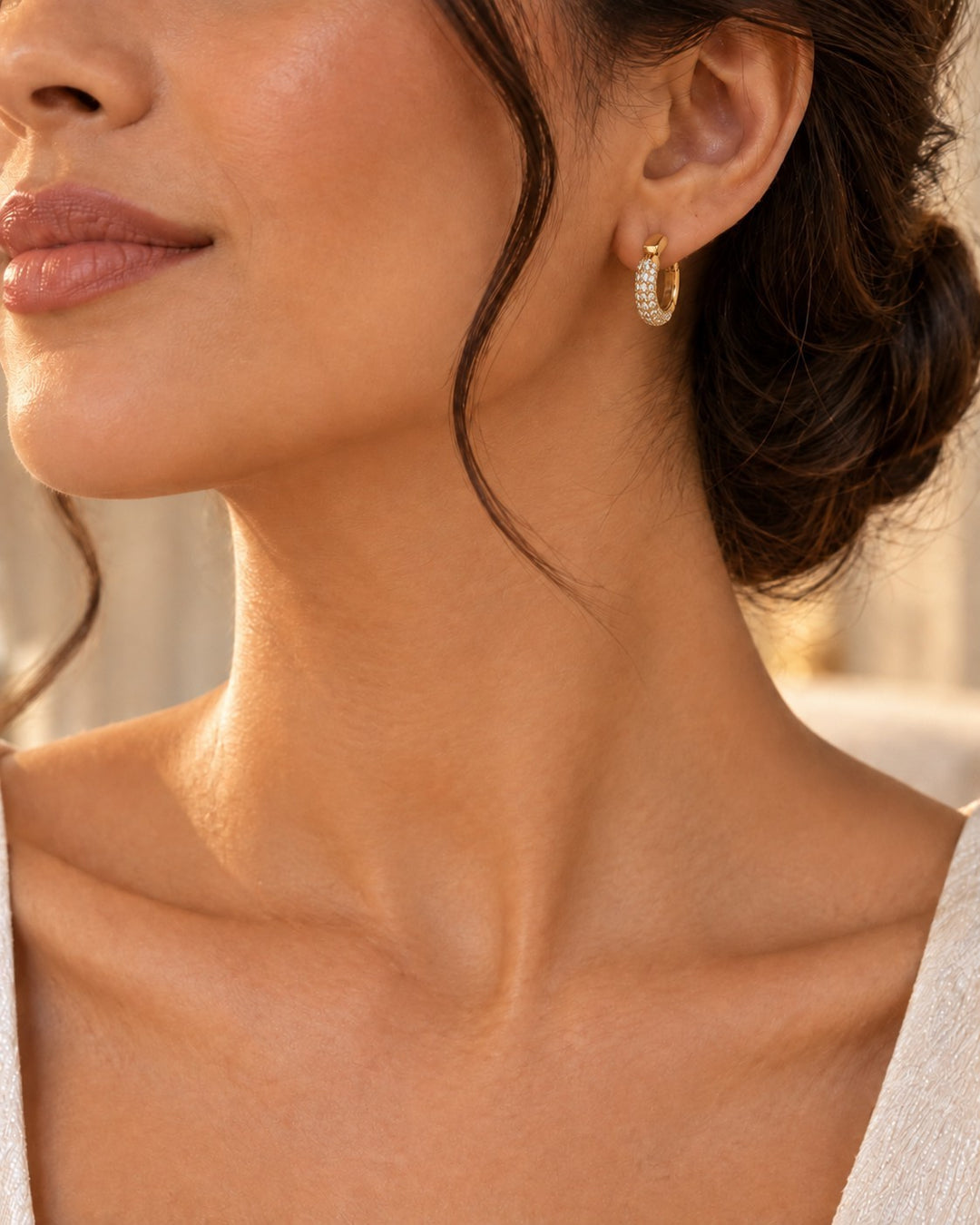 Elli Jewellery gold plated huggie hoop earrings with sparkling diamanté stones worn by a woman