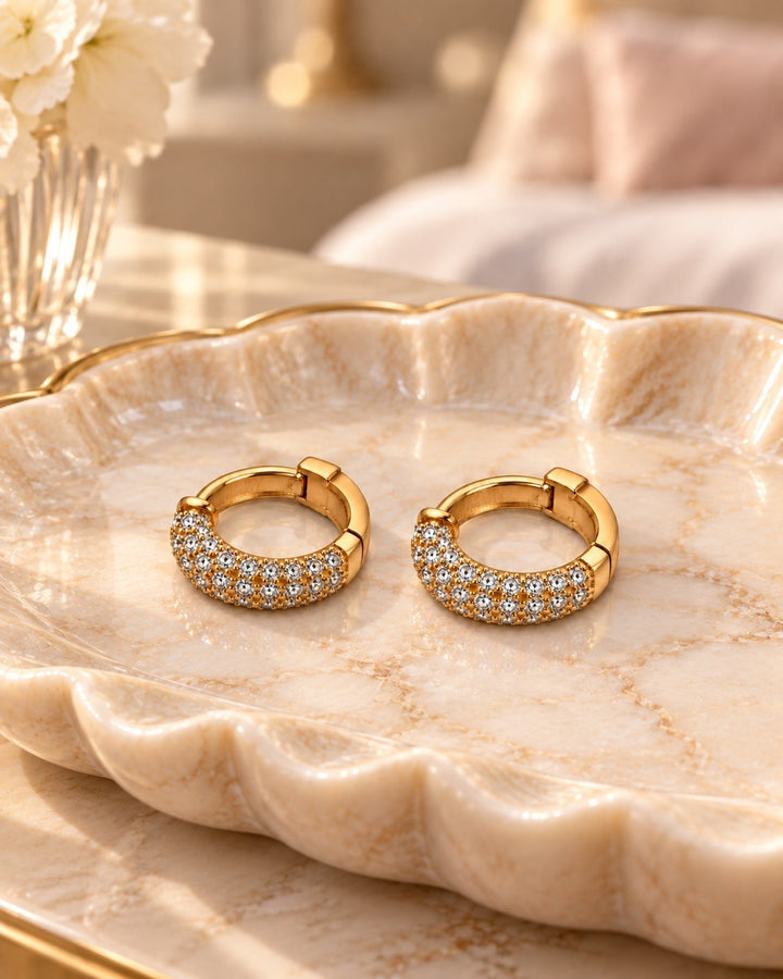 Elli Jewellery gold plated huggie hoop earrings with sparkling diamanté stones resting on a decorative marble tray.