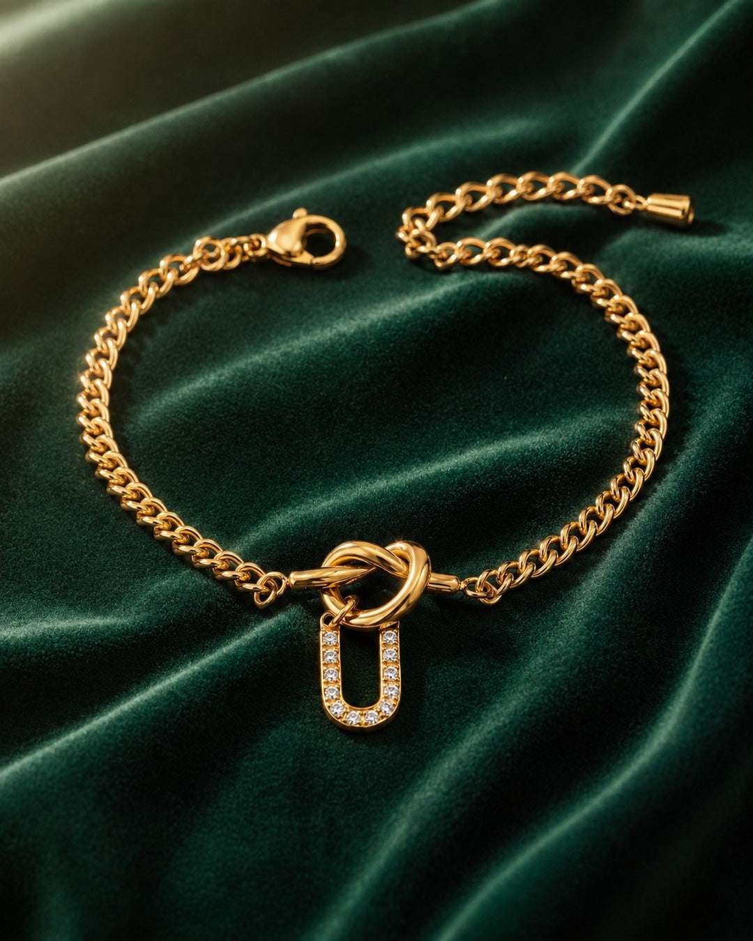Elli Jewellery gold plated chain bracelet featuring a diamante U initial charm on a dark green velvet background