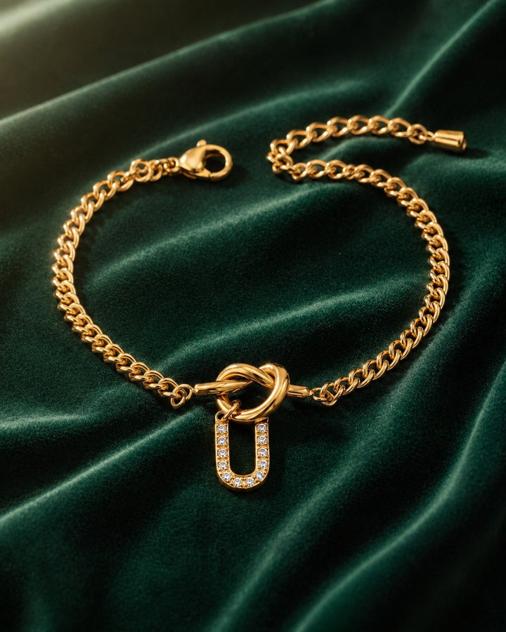 Elli Jewellery gold plated chain bracelet featuring a diamante U initial charm on a dark green velvet background