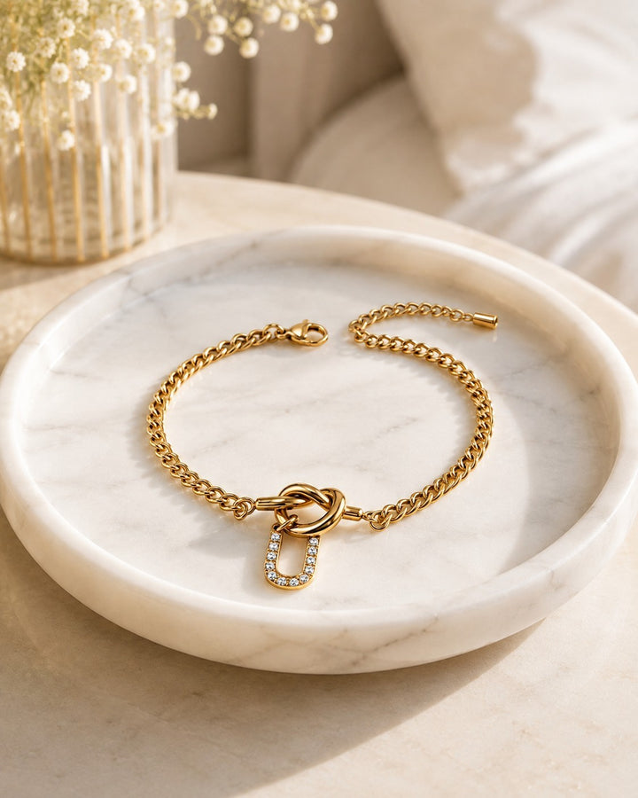 Elli Jewellery gold plated waterproof chain bracelet featuring a diamante U initial charm on a marble tray.