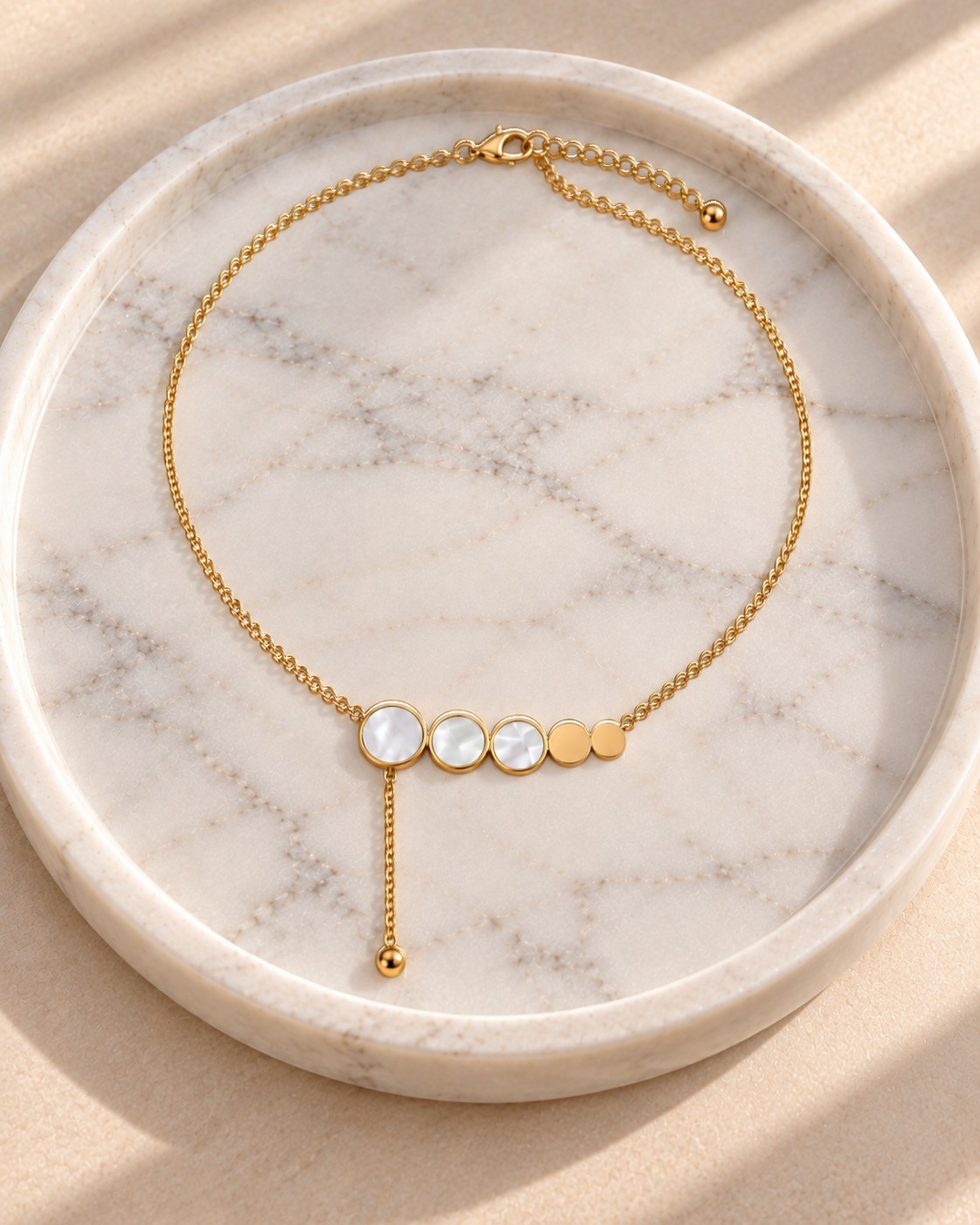 Elli Jewellery gold plated necklace featuring mother of pearl and gold discs on a delicate chain on a marble tray.