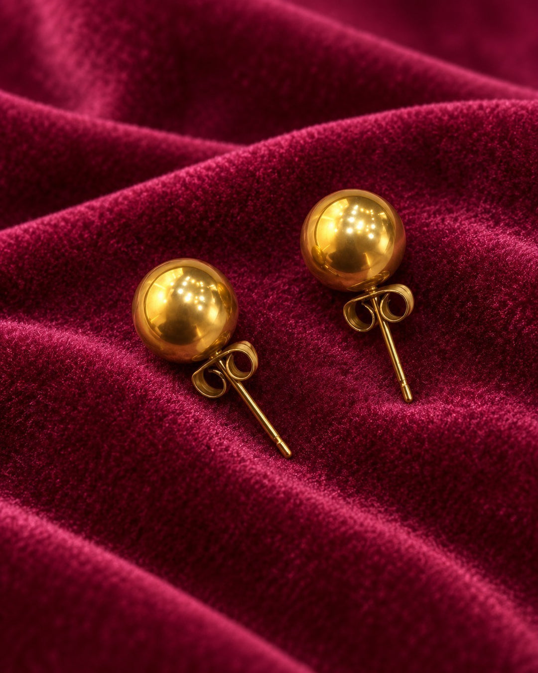 Elli Jewellery 8mm gold plated round dome stud earrings with a polished finish on a deep red velvet background.