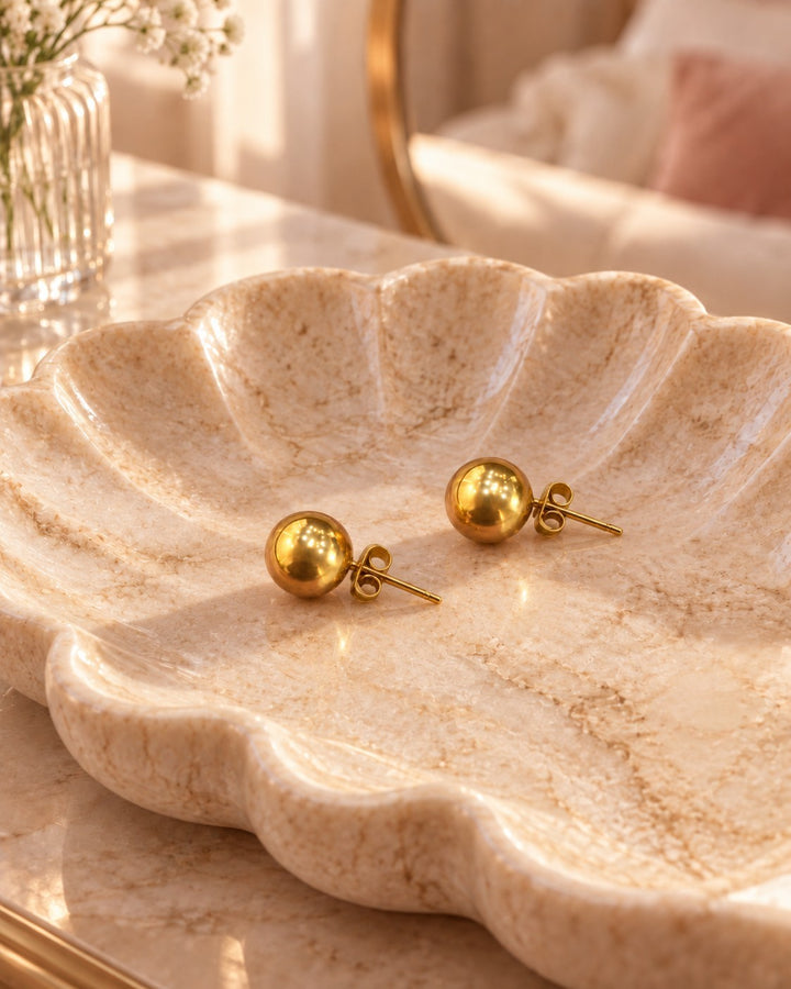 Elli Jewellery gold plated 8mm round dome stud earrings with a polished finish resting in a decorative marble dish.