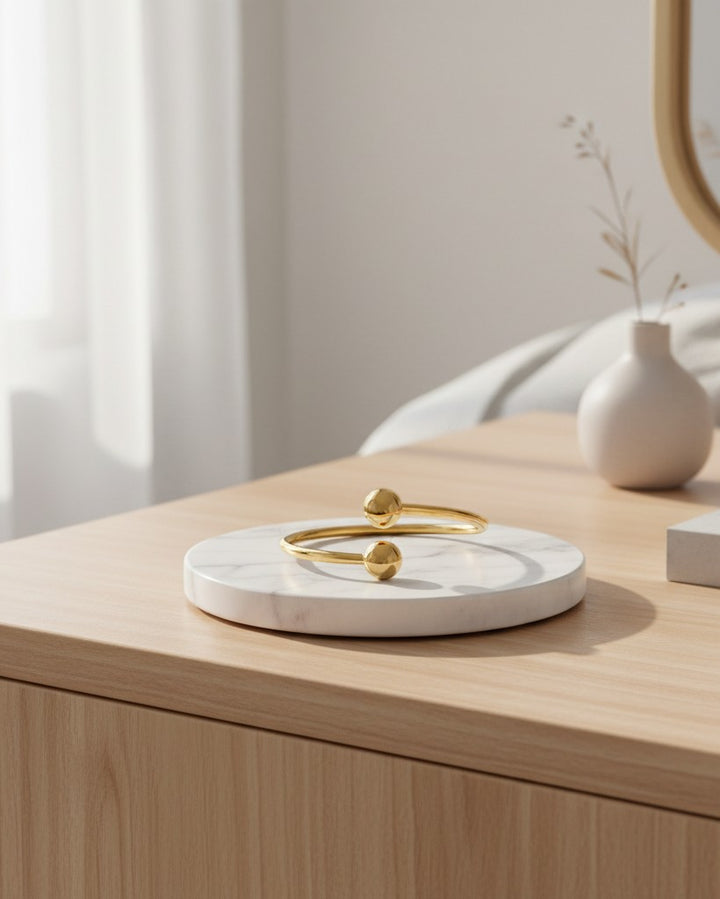 Elli Jewellery gold plated minimalist double ball ring resting on a white marble display stand on a wooden table.