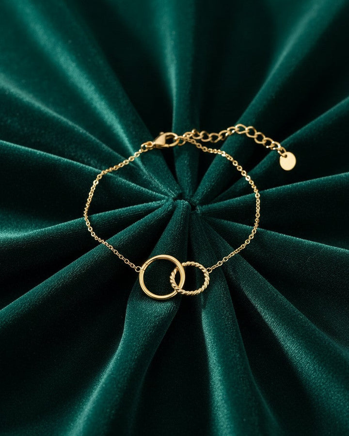 Elli Jewellery gold-toned anklet featuring two interlocking circles on a delicate chain against green velvet fabric.