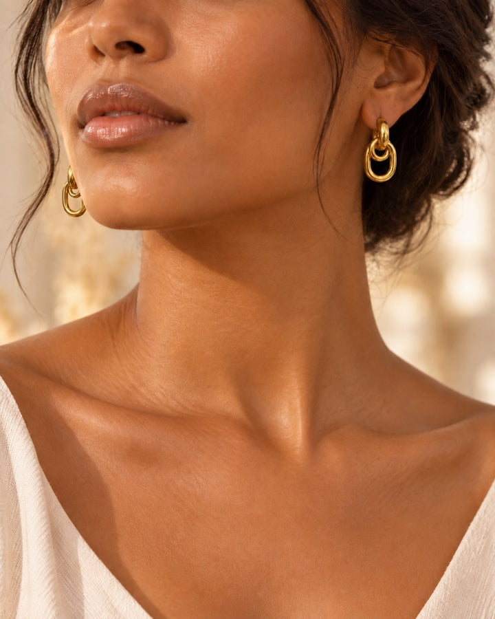 Elli Jewellery gold plated waterproof drop earrings with a modern interlocking oval design worn by a woman.