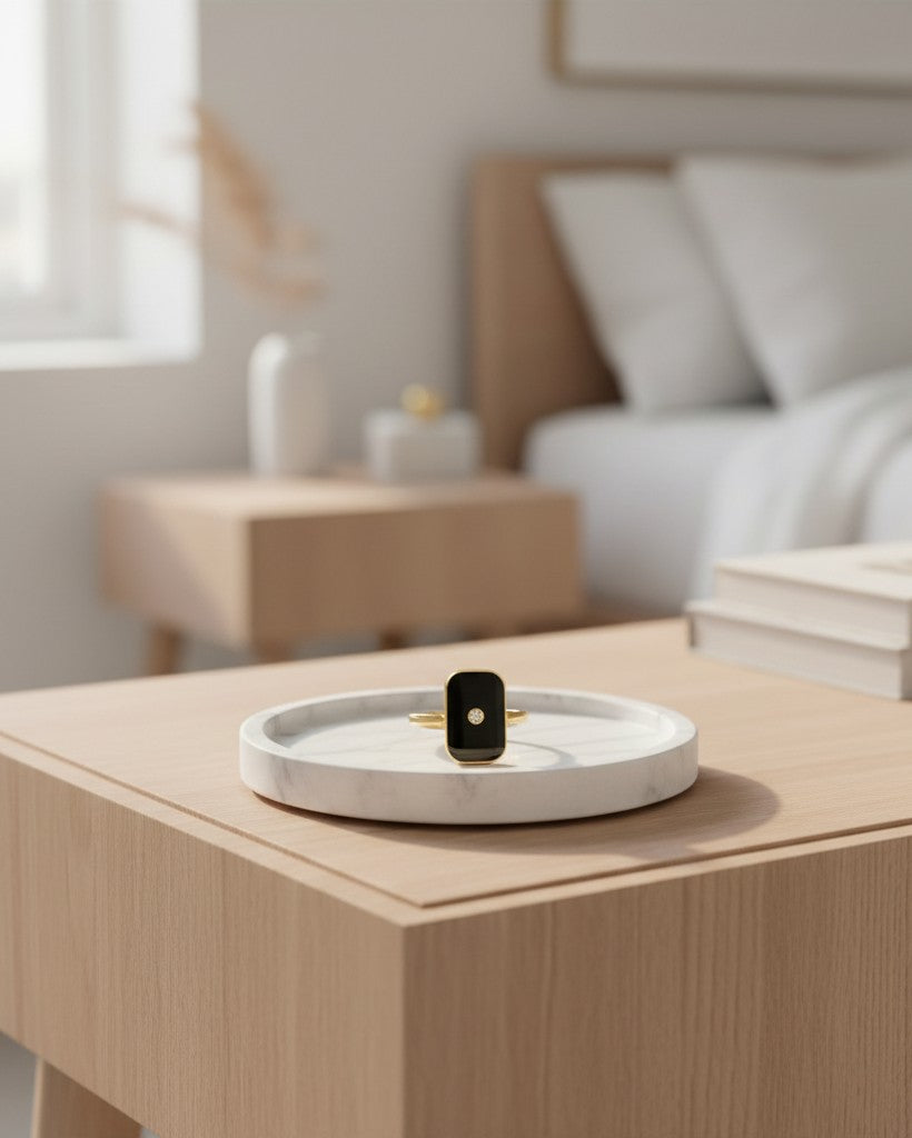 Elli Jewellery gold-plated rectangular statement ring with black enamel and a central stone on a marble tray.