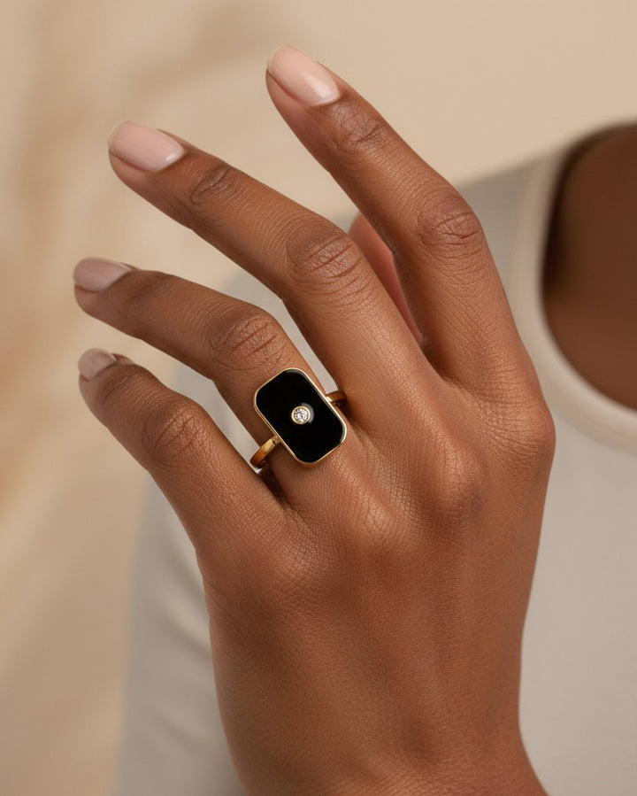 Elli Jewellery gold-plated rectangular statement ring with black enamel and a central stone on a model's finger