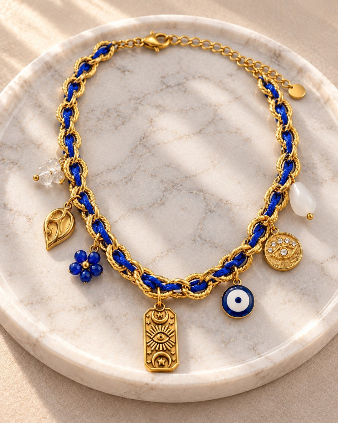 Elli Jewellery gold plated chain necklace with blue cord and multiple charms including an evil eye on marble tray