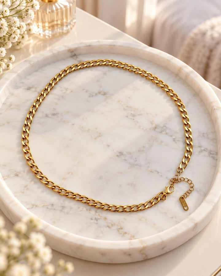 Elli Jewellery gold plated waterproof Figaro chain necklace displayed on a white marble tray with soft lighting.