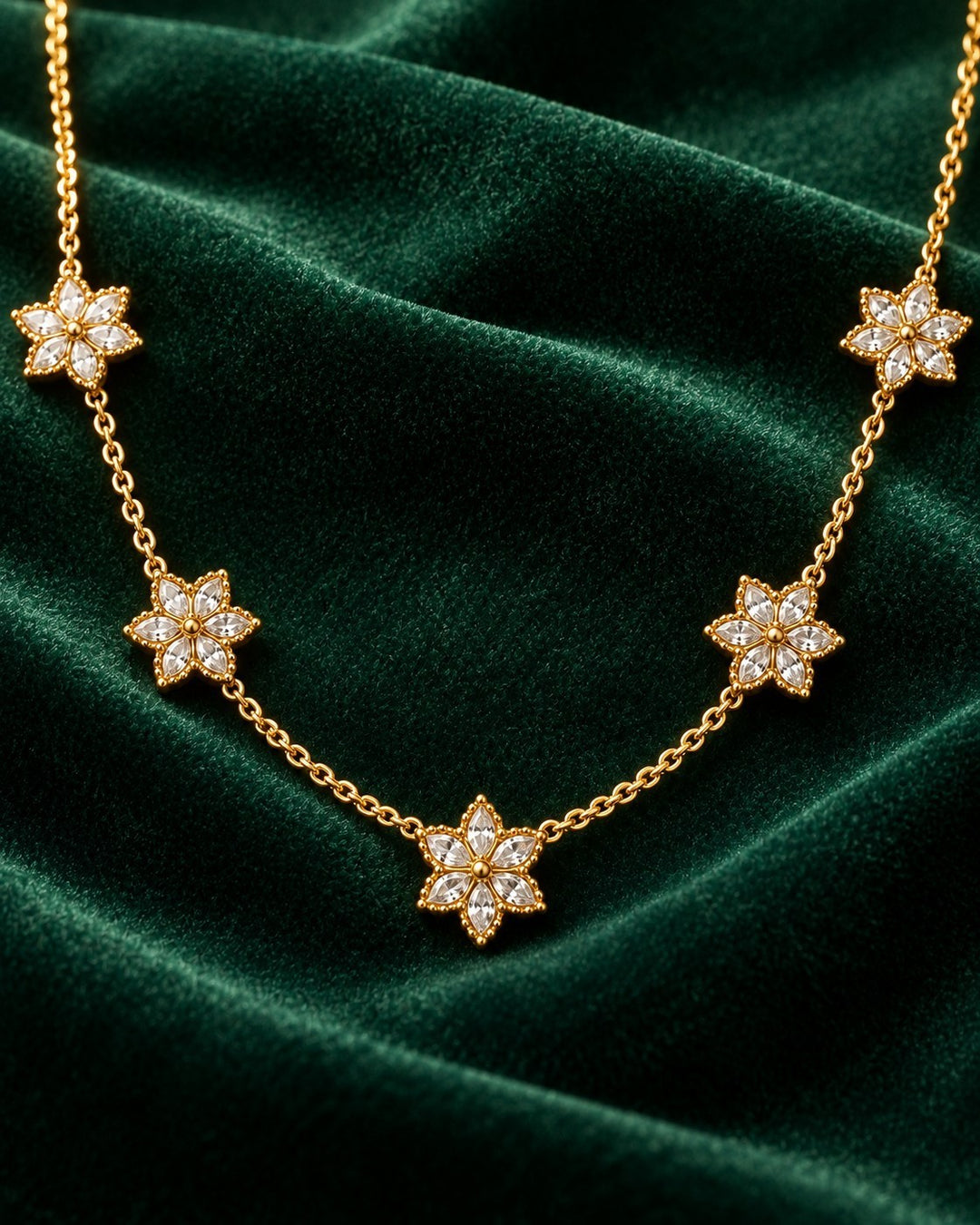 Elli Jewellery gold plated necklace featuring delicate floral bloom pendants with clear stones on a green velvet background