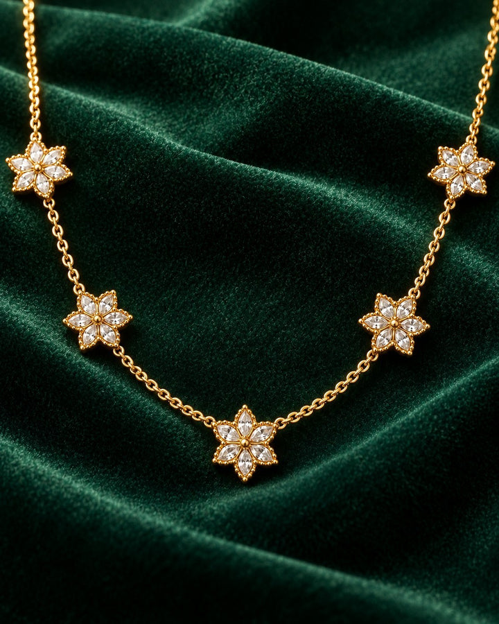 Elli Jewellery gold plated necklace featuring delicate floral bloom pendants with clear stones on a green velvet background